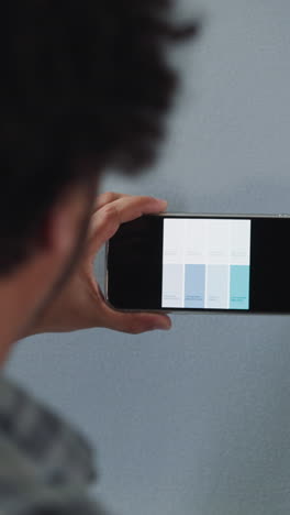 african-american designer chooses color shade for flat wall painting on smartphone screen close back view. black decorator with mobile phone works in premise