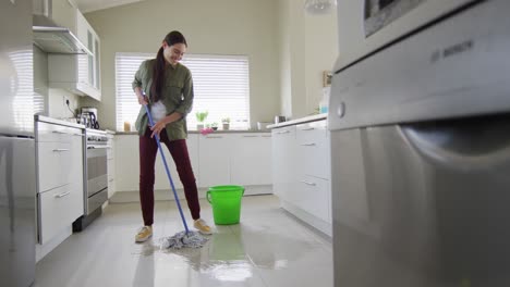 mujer caucásica feliz limpiando el piso con un trapeador y un cubo de agua en casa