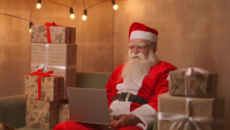 Videollamadas-De-Papá-Noel-Para-Llevar-Al-Niño-En-La-Computadora-Portátil,-Mantener-Presente,-Sentarse-En-La-Mesa-De-Casa.-La-Pandemia-Y-El-Aislamiento-Del-Santa-Felicita-A-Los-Niños-A-Distancia.-Imágenes-4k-De-Alta-Calidad