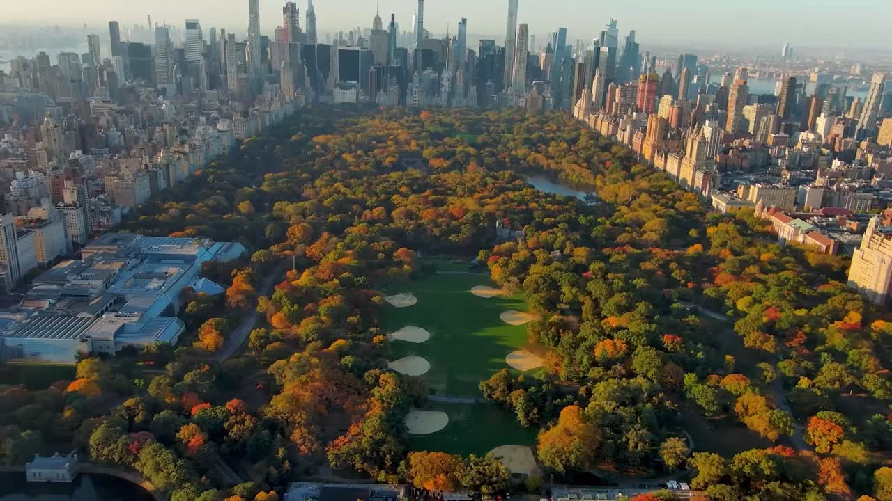Riprese aeree di Central Park a New York City durante l'autunno, circondato da un denso skyline urbano di grattacieli. Gli alberi del parco mostrano un vibrante fogliame stagionale in varie tonalità.
