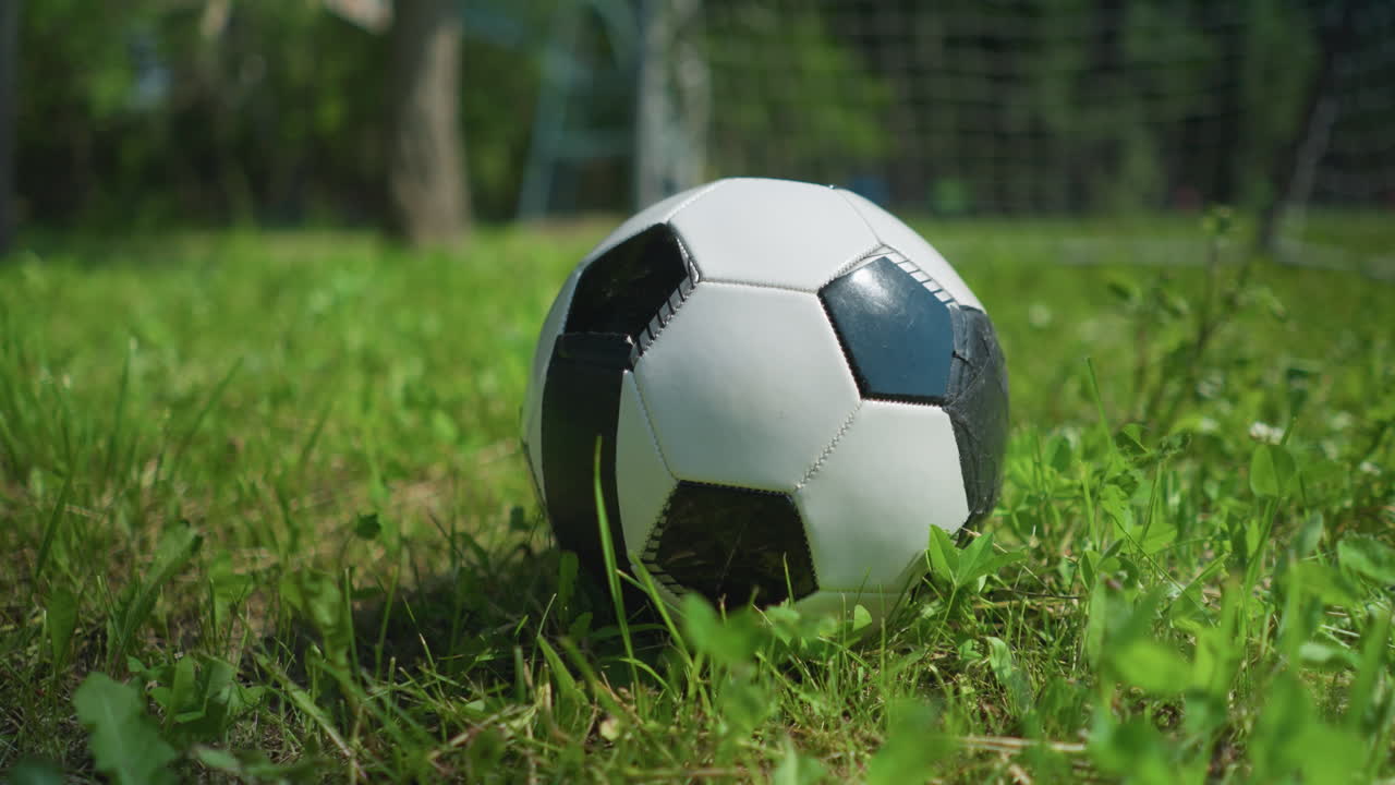 Close-up view of a soccer ball resting on a grassy field with a blur view of a little child running with a ball in his hand in the background