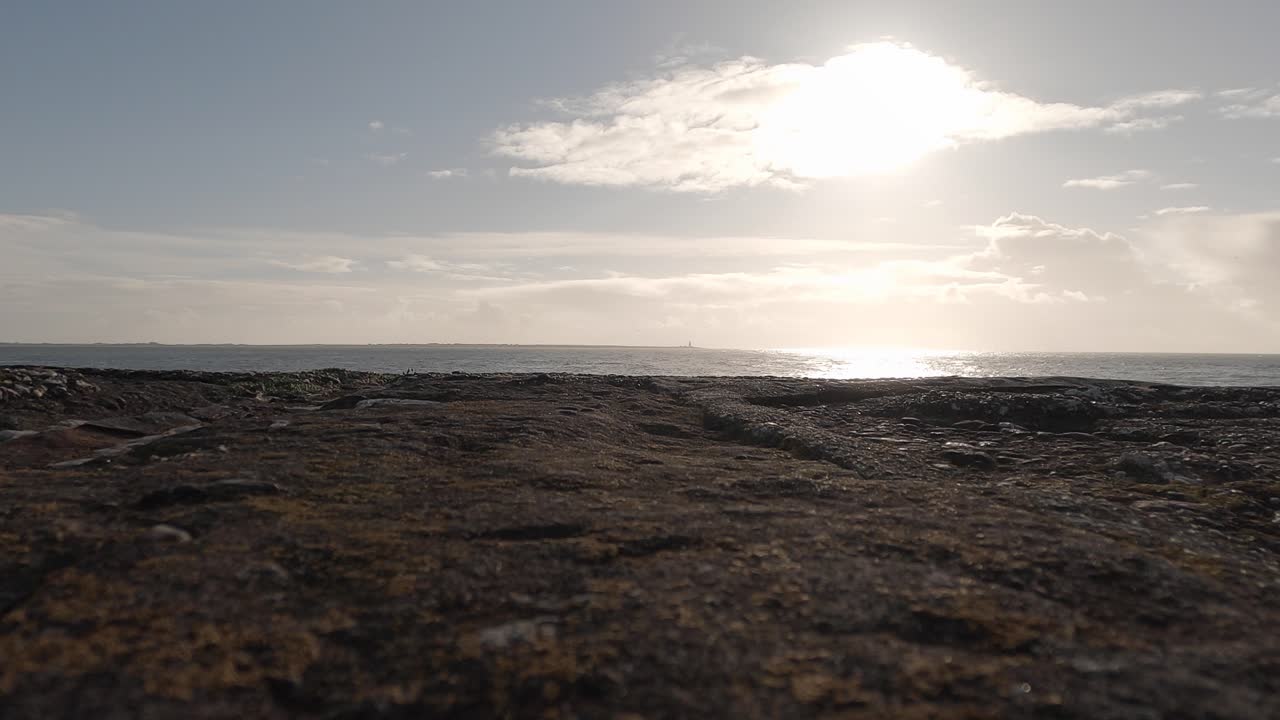Ocean horizon splits frame, rocky beach foreground, distant lighthouse