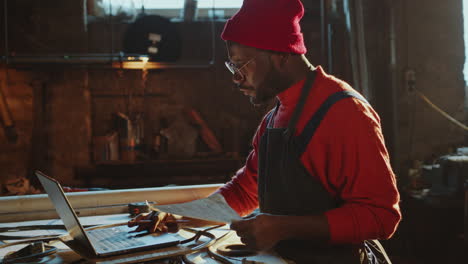 african american blacksmith drawing sketch and using laptop in workshop