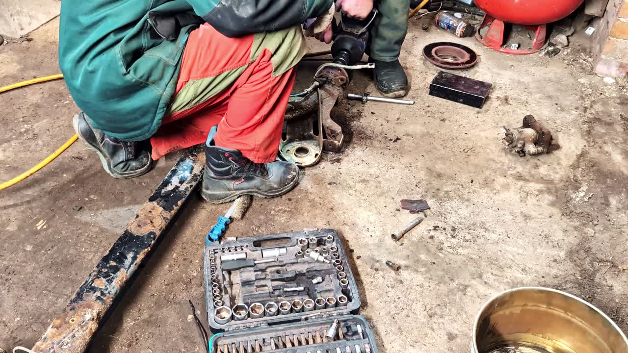 Mechanics repairing vehicle suspension part on dirty workshop floor with tool kit