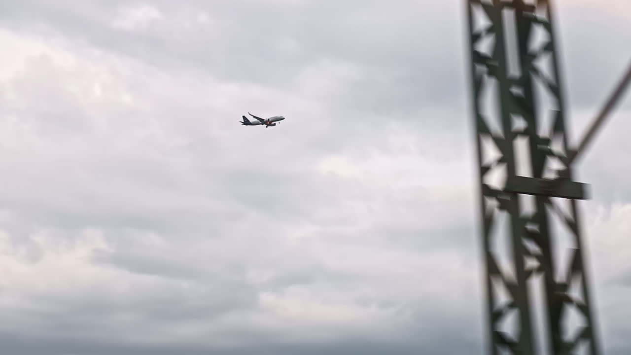 Airplane captured mid-flight through train window under overcast sky