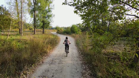 Chica-Con-Casco-Montando-Una-Bicicleta-De-Montaña-Y-Montando-En-Un-Camino-Rural-En-El-Bosque,-Drone-Sigue-4k