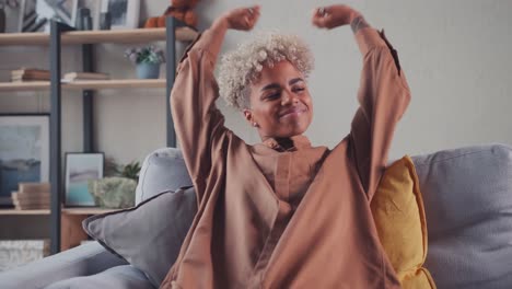 african woman resting on couch taking deep breath holding hands behind head