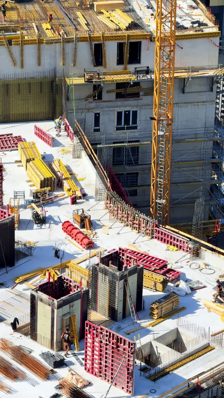 High-rise construction update. Construction workers are busy at a high-rise site with cranes, materials, and concrete forms under a clear blue sky