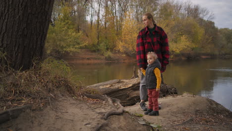 single mother is walking with little son at nature resting at woodland walking together at autumn day viewing small river in forest