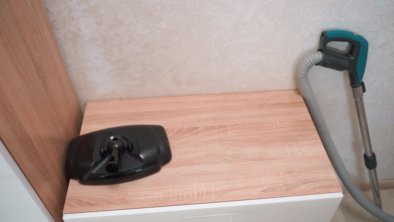 Accessori per aspirapolvere disposti su uno scaffale di legno, tecnico che prepara il kit di pulizia e posiziona gli ugelli accanto al tubo, superficie laminata ordinata, ispezione ravvicinata dei connettori, scena di tranquilla manutenzione domestica