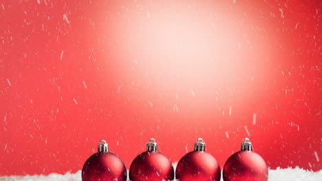 animation of snow falling over red baubles against copyspace on red gradient background