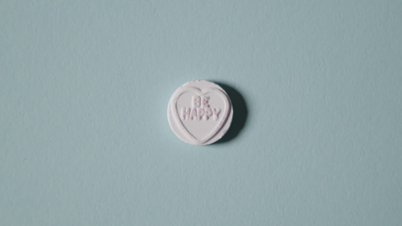 mano recogiendo caramelos de corazón con un mensaje de felicidad sobre fondo azul