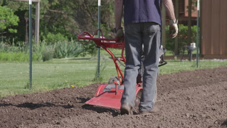 el hombre usa un rototiller en la primavera para preparar su jardín