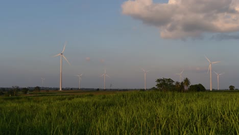 Turbinas-Eólicas-Salen-Disparadas-De-Una-Tierra-De-Cultivo-Mientras-El-Sol-Se-Pone-Mientras-Los-Camiones-Pasan-Haciendo-Nubes-De-Polvo,-Energía-Alternativa-Limpia-En-Tailandia-Y-El-Sudeste-Asiático-Continental