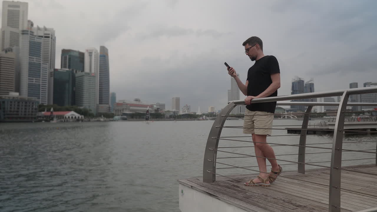 Man using smartphone on a waterfront pier in Singapore