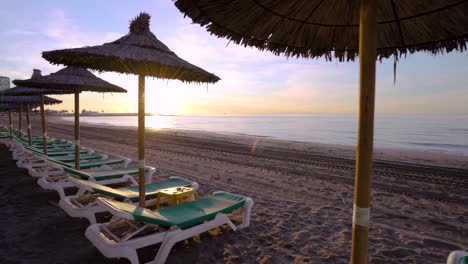 Amanecer-En-Constante-Movimiento-En-La-Playa-De-Marbella-Con-Sombrillas,-Destino-De-Vacaciones-De-Ensueño,-Toma-Suave-De-Cardán-De-4k