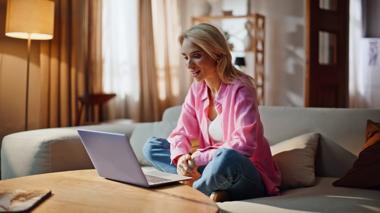 Girl enjoying video conference by laptop in apartment. Blonde woman online call