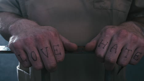 extreme close-up shot of a prisoner's hands with "love" and "hate" tattooed across his fingers as he clutches the bars of his prison cell while the camera does a parallax move