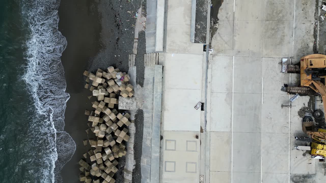 Bird's Eye Top Down View of Island Town boulevard with concrete tetrapods on the shoreline and ocean waves crashing