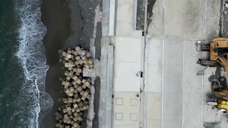 bird's eye top down view of island town boulevard with concrete tetrapods on the shoreline and ocean waves crashing