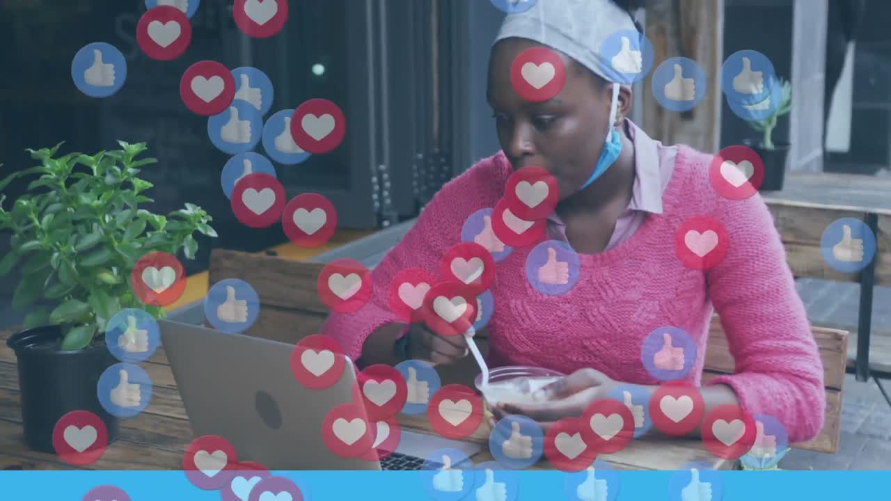 Animace ikon „To se mi líbí“ a srdíček ze sociálních médií nad Afroameričankou s notebookem jící v kavárně.