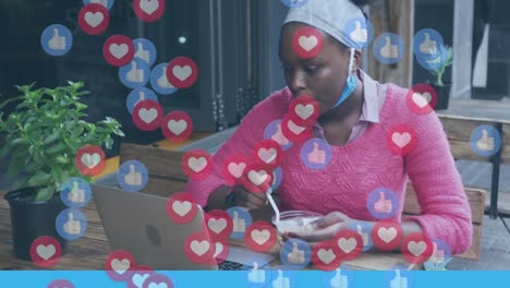 Animation-of-social-media-like-and-love-icons-over-african-american-woman-with-laptop-eating-at-cafe