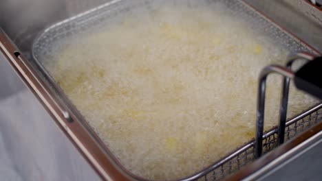 raw frozen potato being deep-fried in wire basket