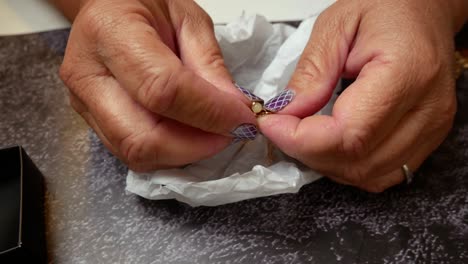 Close-up-of-fingers-unhooking-a-necklace-that-has-just-been-taken-out-of-a-tissue-paper