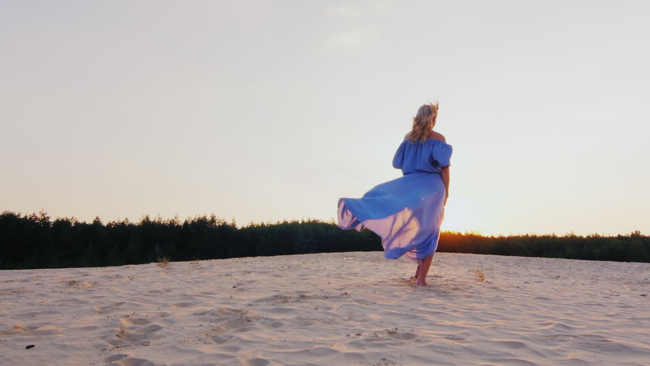 가벼운 옷을 입은 젊은 여성이 해변에서 석양을 질주합니다.