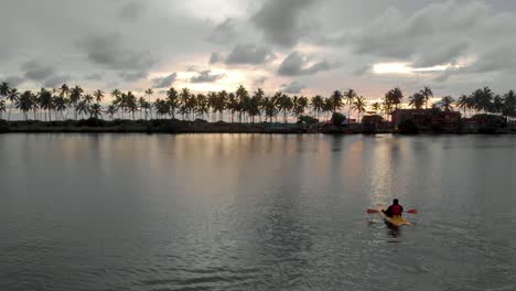 4k-Aerial-Fly-by-Drone-Reveal-shot-of-a-28-year-old-Indian-male-kayaking-in-the-backwaters-of-Varkala-during-sunset,-Kerala