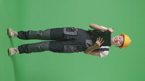 cuerpo lleno de trabajadora asiática que usa gafas de protección y casco de seguridad tomando nota en una tableta mientras está de pie en el estudio de fondo de la pantalla verde