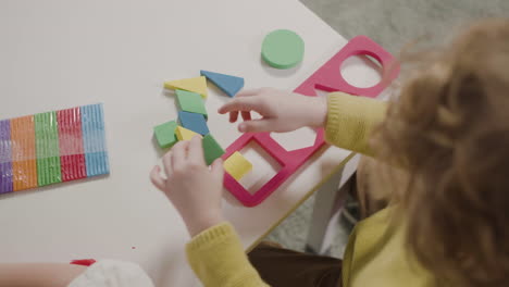 bovenaanzicht van een kleine jongen die speelt met een vormensorteerder terwijl hij aan een bureau zit in een montessorischool