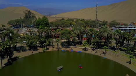 aerial shot over huacachina oasis in the desert with a slow tilt up shot along the water's edge with palm trees