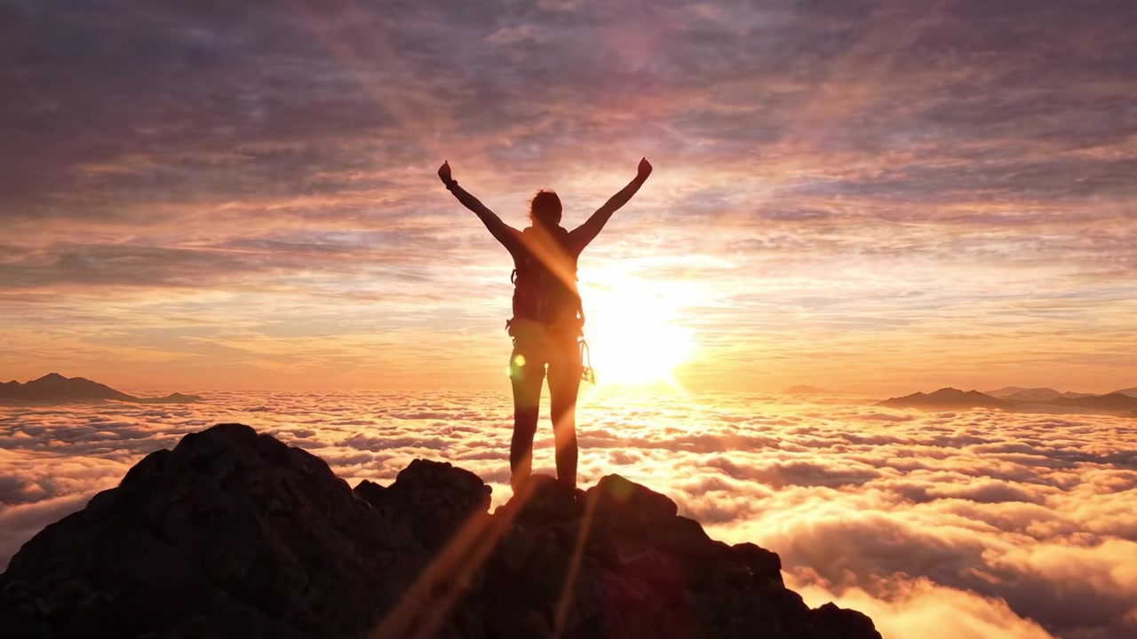 Un escalador triunfante celebra en la cima, con los brazos en alto contra el impresionante telón de fondo de un amanecer vibrante que ilumina un mar de nubes.