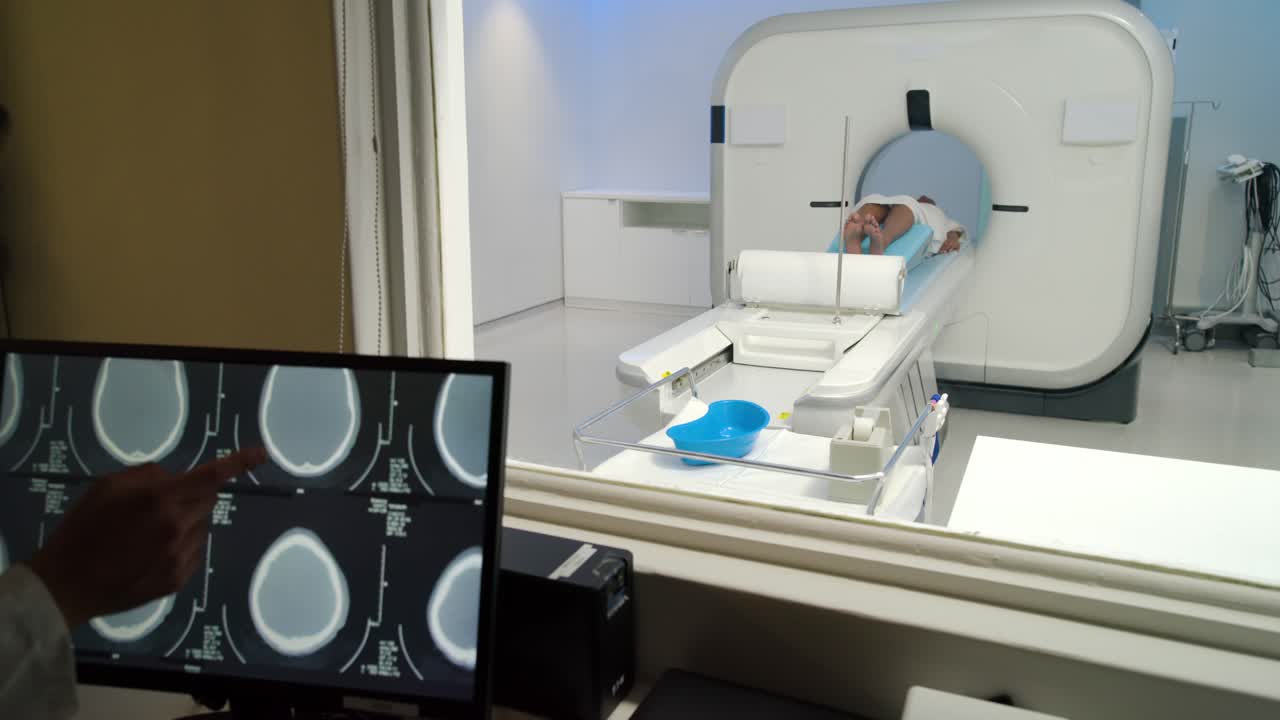 Il tecnico è alla console e avvia la scansione mentre visualizza le scansioni cerebrali; il paziente resta immobile