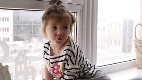 a little girl is sitting on the windowsill, the cat is looking at her from the floor