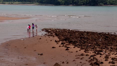 Mom-holding-her-three-kids'-hands-walking-together-towards-the-sea