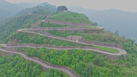 a serpentine road curves gracefully through vibrant green mountains, offering a breathtaking view of natural beauty and human engineering in harmony, captured from a high-altitude aerial perspective.