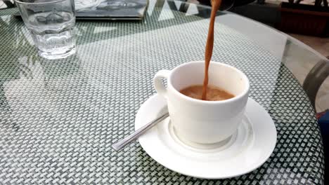 Tee-Oder-Indischer-Masala-Chai-Wird-Umgekehrt-Gegossen,-Während-Eine-Weiße-Tasse-Auf-Einem-Cafétisch-Leer-Wird