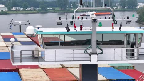 large cargo ship navigating a river with colorful containers and houses in the background