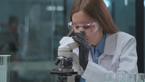 young woman is viewing analysis in microscope in laboratory medical and virology research of coronavirus health professional looking for a curing