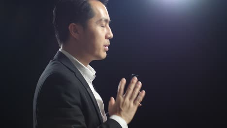 close up side view of asian speaker man in business suit holding and pointing smartphone while speaking in the black screen studio