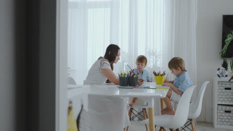 Two-children-of-boys-draw-with-his-mother-sitting-in-the-kitchen.-Happy-family-at-home.