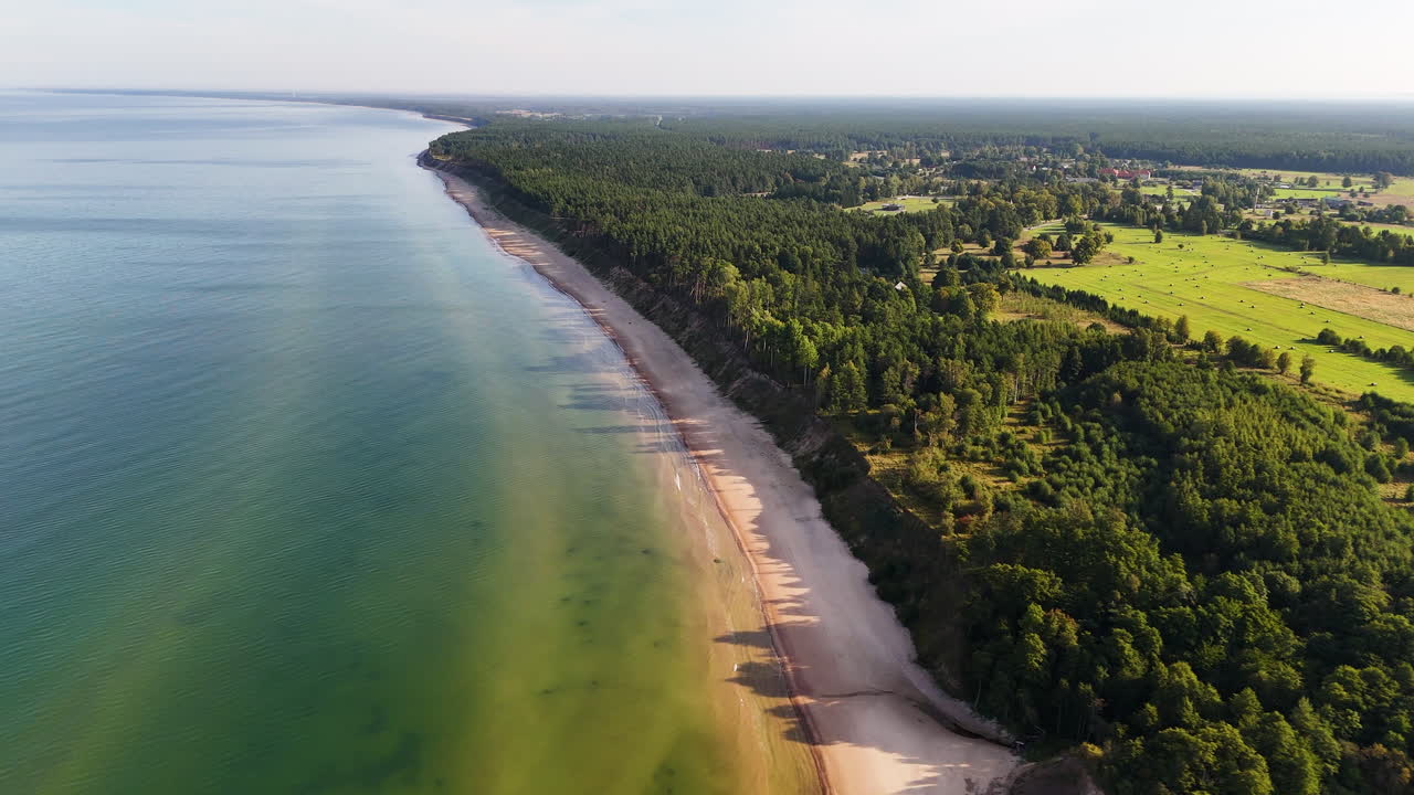 Aerial view of Baltic Sea coastline bordered by green farmland in Jurkalne, Latvia.