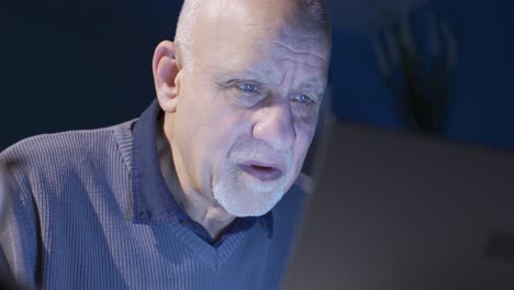 Old-man-looking-at-laptop-at-night-working-seriously-and-focused.