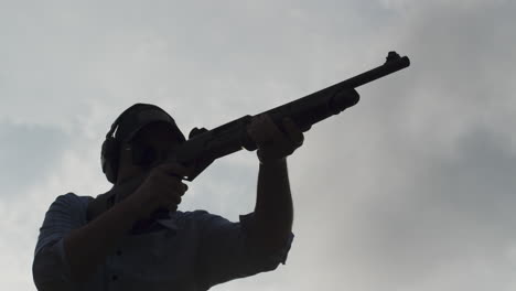 man fires pump-action shotgun in silhouette