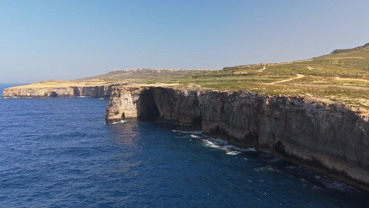 Wied il-Mielaħ a Gozo, Malta, con un arco di roccia naturale, grotte marine e scogliere costiere frastagliate sopra le acque blu del Mediterraneo, ripreso con una vista panoramica da drone.