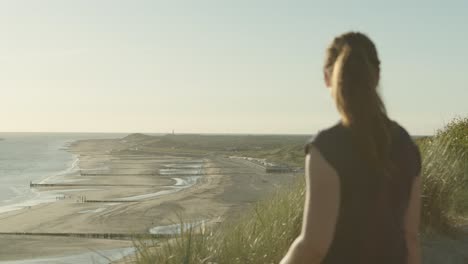 mujer con gafas de sol en la parte superior de la duna viendo la playa de zoutelande