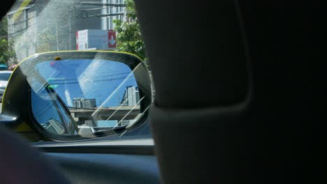pov of side mirror of the moving car while while driving along the city of bangkok, thailand