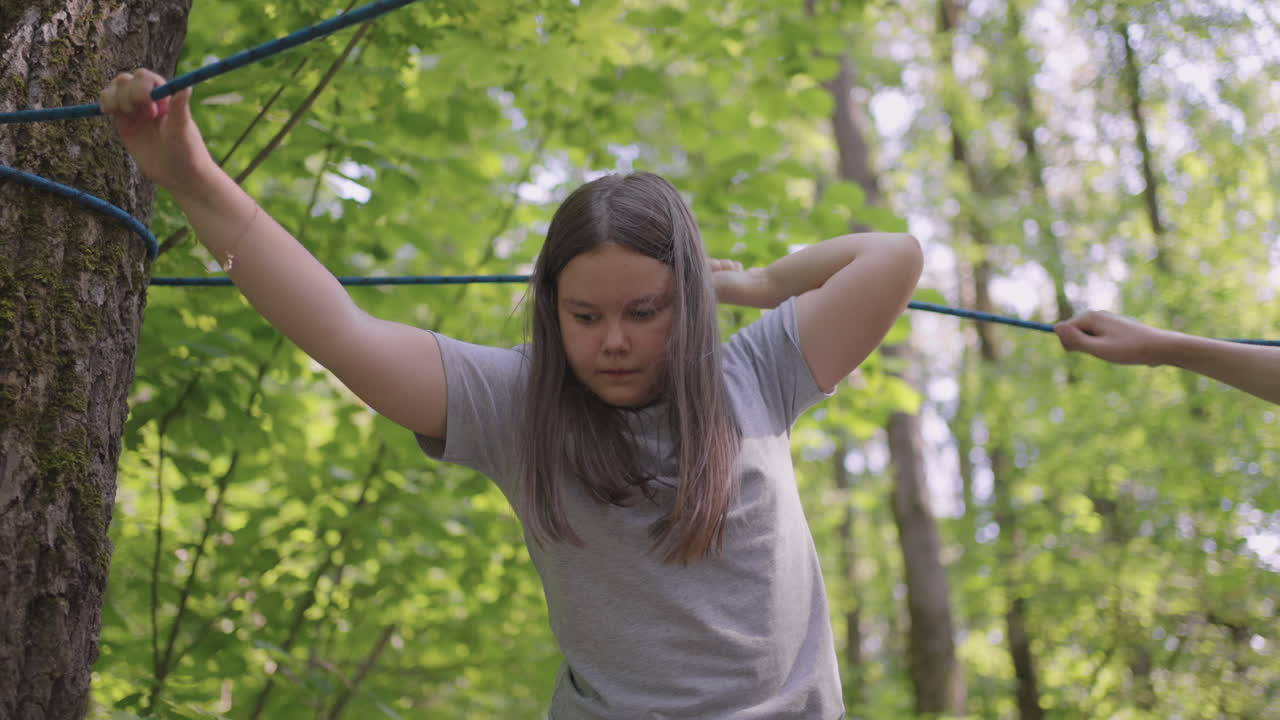 적극적인 아이는 두려움없이 나무 사이의 로프를 오릅니다. 모험 공원의 소녀는 로프 로드에서 장애물을 통과합니다. 어린이 캠프 여름 캠프